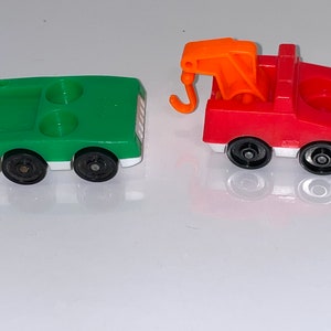 May include: A red toy tow truck with an orange hook and a green toy car. Both toys have black wheels and white accents.