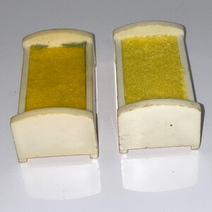 May include: Two white plastic doll beds with yellow fabric mattresses. The beds are small and would be suitable for a dollhouse.