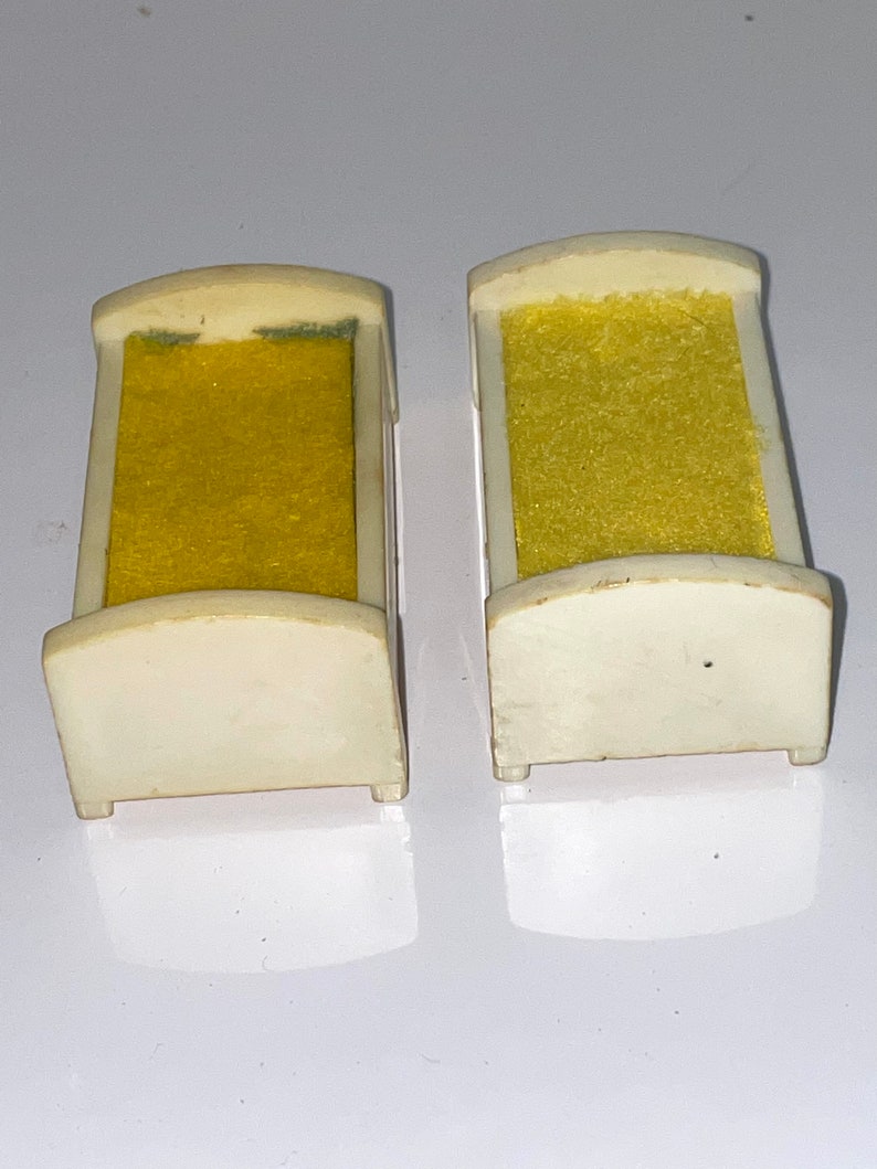 May include: Two white plastic doll beds with yellow fabric mattresses. The beds are small and would be suitable for a dollhouse.