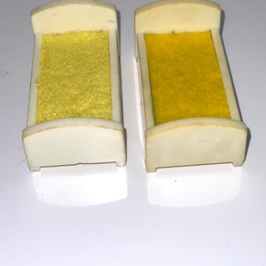 May include: Two white plastic doll beds with yellow fabric mattresses. The beds are about 4 inches long.