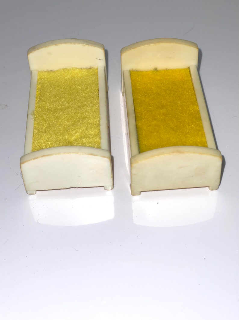 May include: Two white plastic doll beds with yellow fabric mattresses. The beds are about 4 inches long.