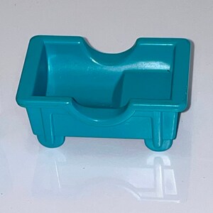 May include: A teal blue plastic toy bed with a rounded headboard and two small wheels on the bottom.