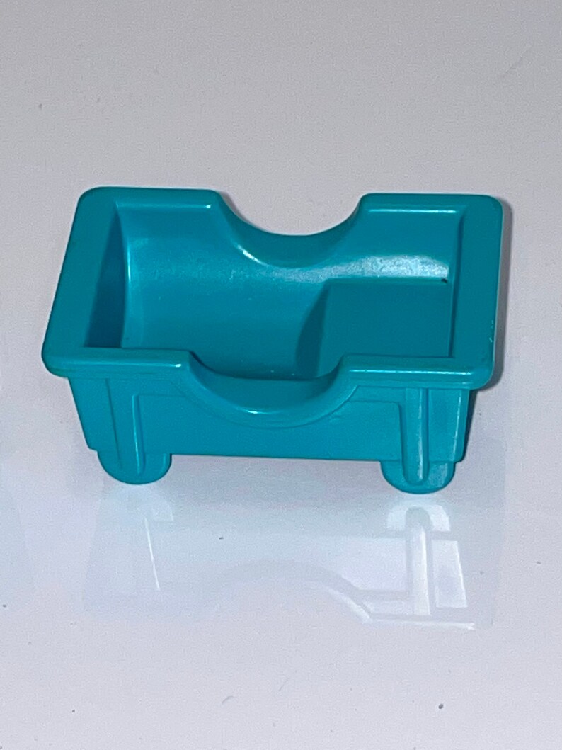 May include: A teal blue plastic toy bed with a rounded headboard and two small wheels on the bottom.