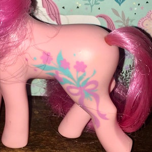 Puede incluir: Pony rosa My Little Pony con un dise&ntilde;o floral morado y azul en un lado. El pony tiene una melena y cola rosadas.