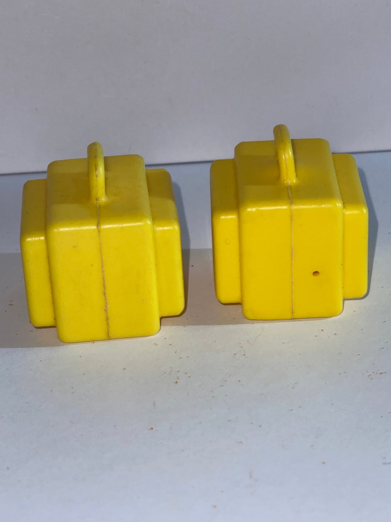 K&ouml;nnte beinhalten: Zwei gelbe Spielzeugkoffer aus Plastik mit Griffen oben. Die Koffer sind etwa 5 cm hoch und 4 cm breit.