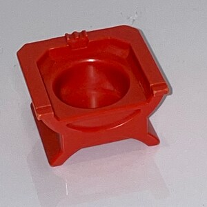 May include: A red plastic toy throne with a small, round seat. The throne has a simple design with a square base and four legs.