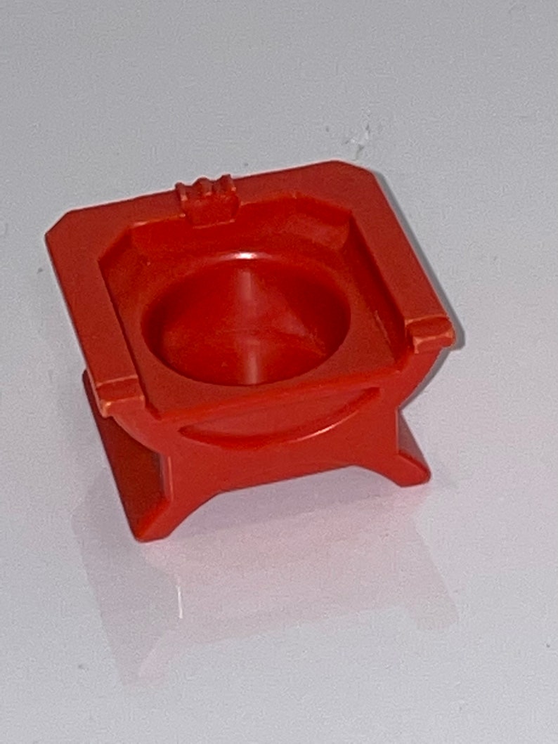 May include: A red plastic toy throne with a small, round seat. The throne has a simple design with a square base and four legs.