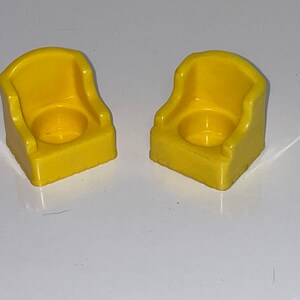 May include: Two yellow plastic chairs with a rounded back and a square base. The chairs are designed for small children.