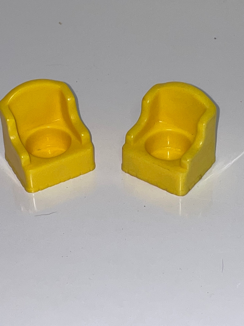 May include: Two yellow plastic chairs with a rounded back and a square base. The chairs are designed for small children.