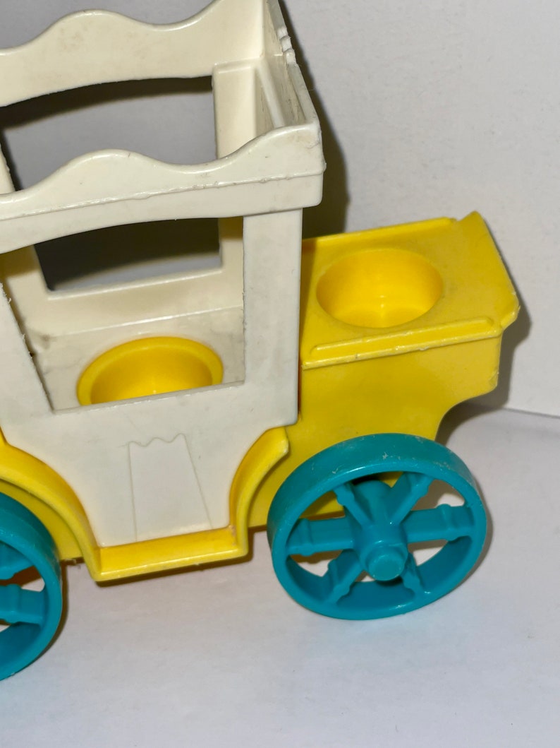 May include: A yellow and white plastic toy carriage with blue wheels. The carriage has two yellow cup holders and a white roof.