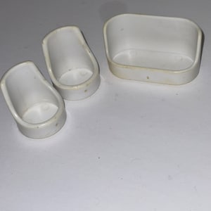 Puede incluir: Un conjunto de tres muebles de casa de mu&ntilde;ecas de pl&aacute;stico blanco: dos sillas y un sof&aacute;.