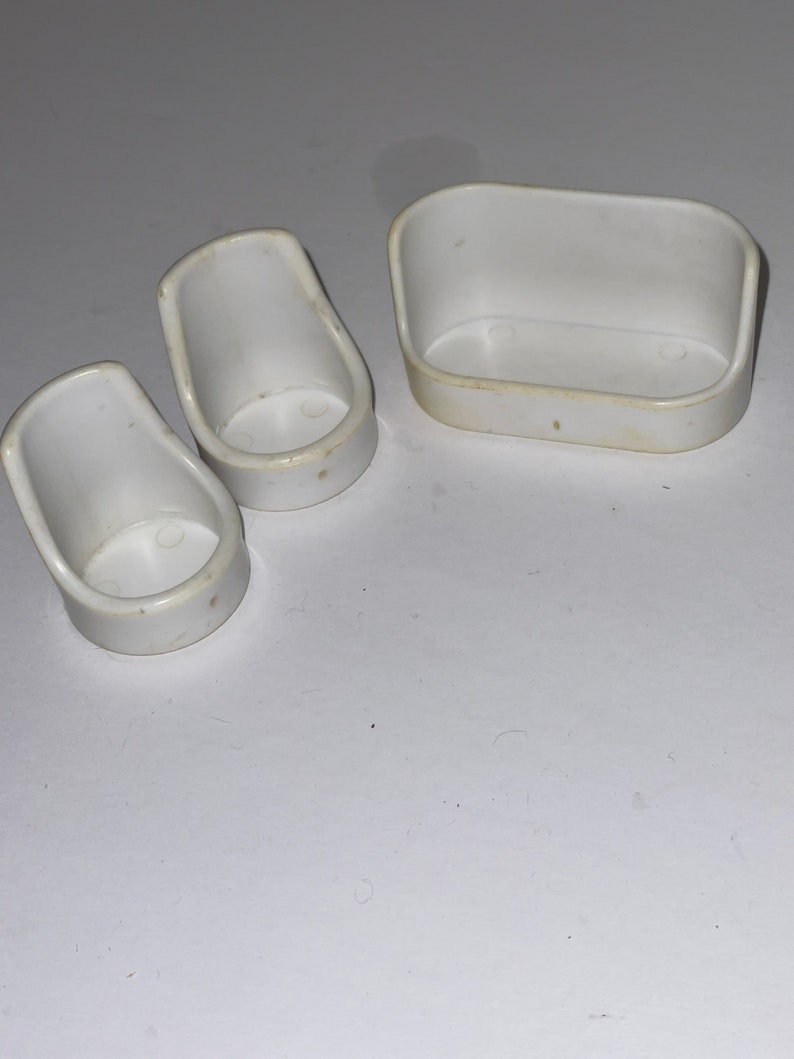 Puede incluir: Un conjunto de tres muebles de casa de mu&ntilde;ecas de pl&aacute;stico blanco: dos sillas y un sof&aacute;.