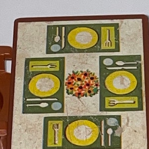 May include: A brown plastic play table with a white and brown marbled surface. The table has a green and yellow design with four place settings, each with a plate, fork, knife, and spoon. A floral centerpiece is in the center of the table.