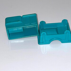 May include: Two teal blue plastic toy truck bed pieces. One piece is a flat bed and the other piece has a raised cab area.