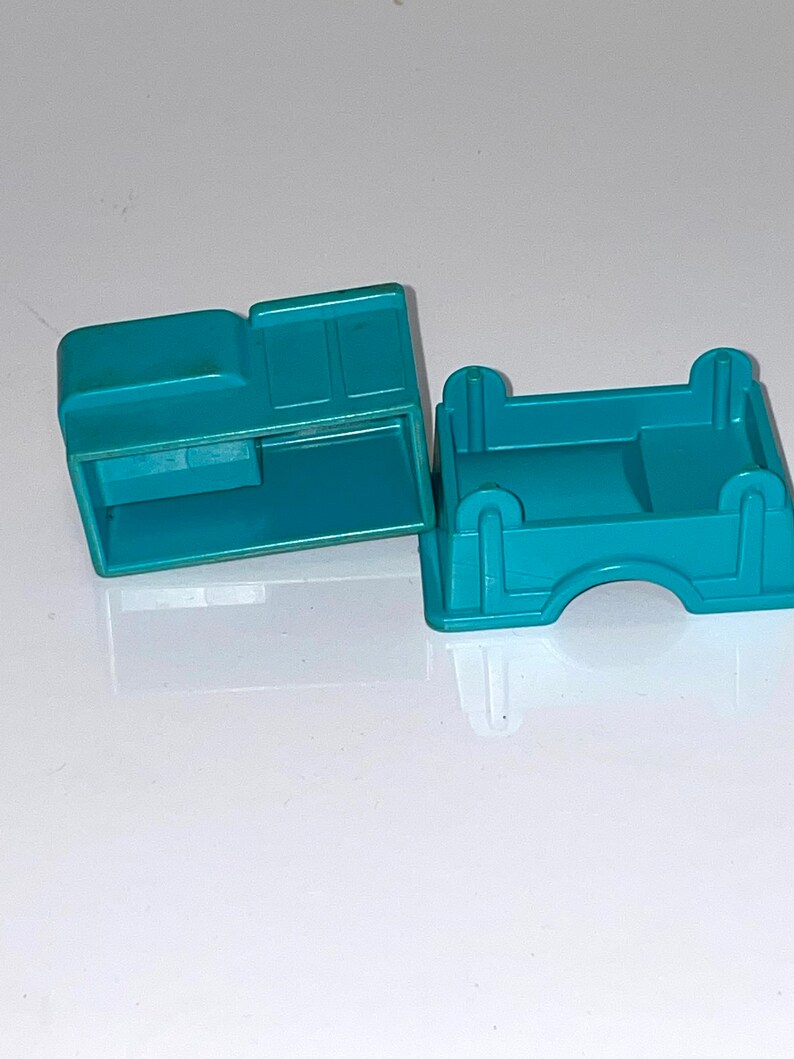 May include: Two teal blue plastic toy truck bed pieces. One piece is a flat bed and the other piece has a raised cab area.