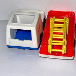 May include: Two vintage toy vehicles, a white mail truck with blue accents and a red fire truck with a yellow ladder. The mail truck has the word "MAIL" printed on the side.