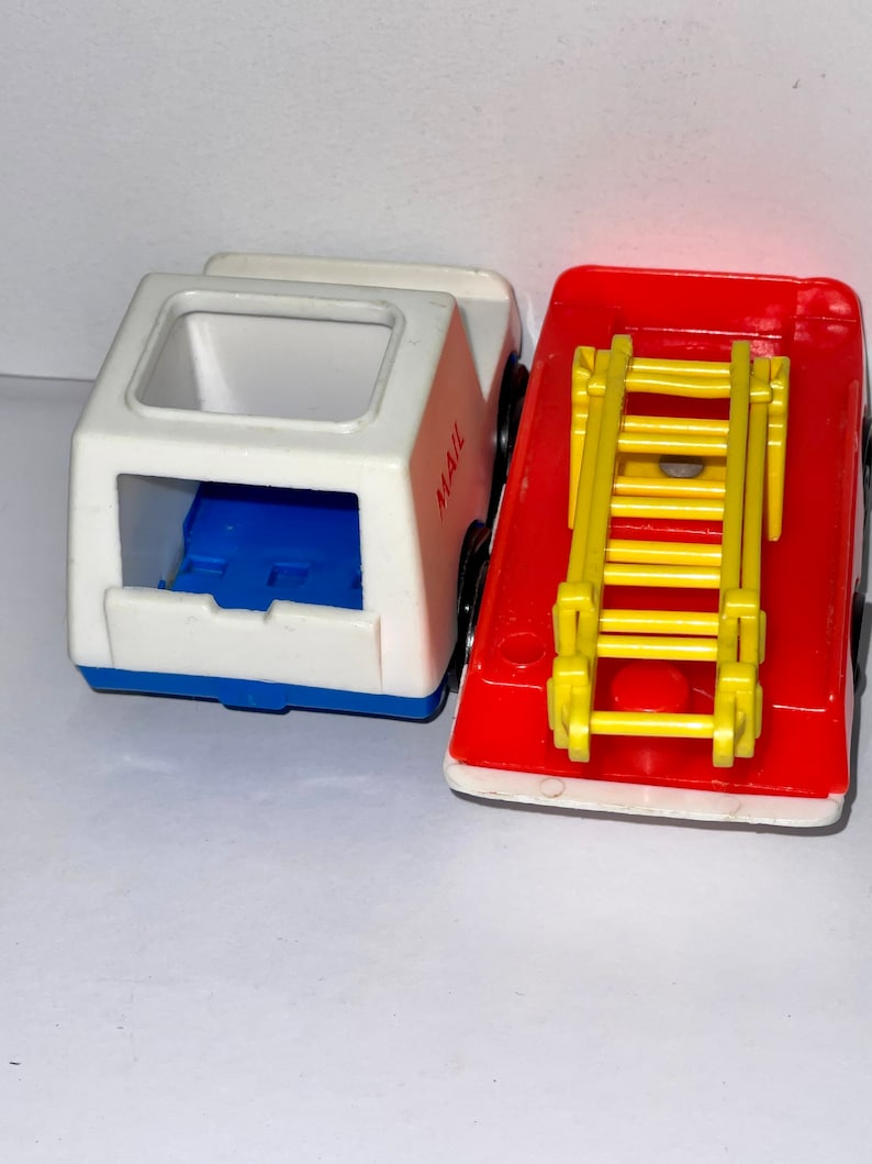 May include: Two vintage toy vehicles, a white mail truck with blue accents and a red fire truck with a yellow ladder. The mail truck has the word "MAIL" printed on the side.