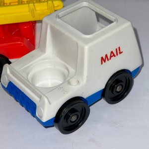 May include: White plastic toy mail truck with blue trim and black wheels. The truck has a red "MAIL" label on the side.
