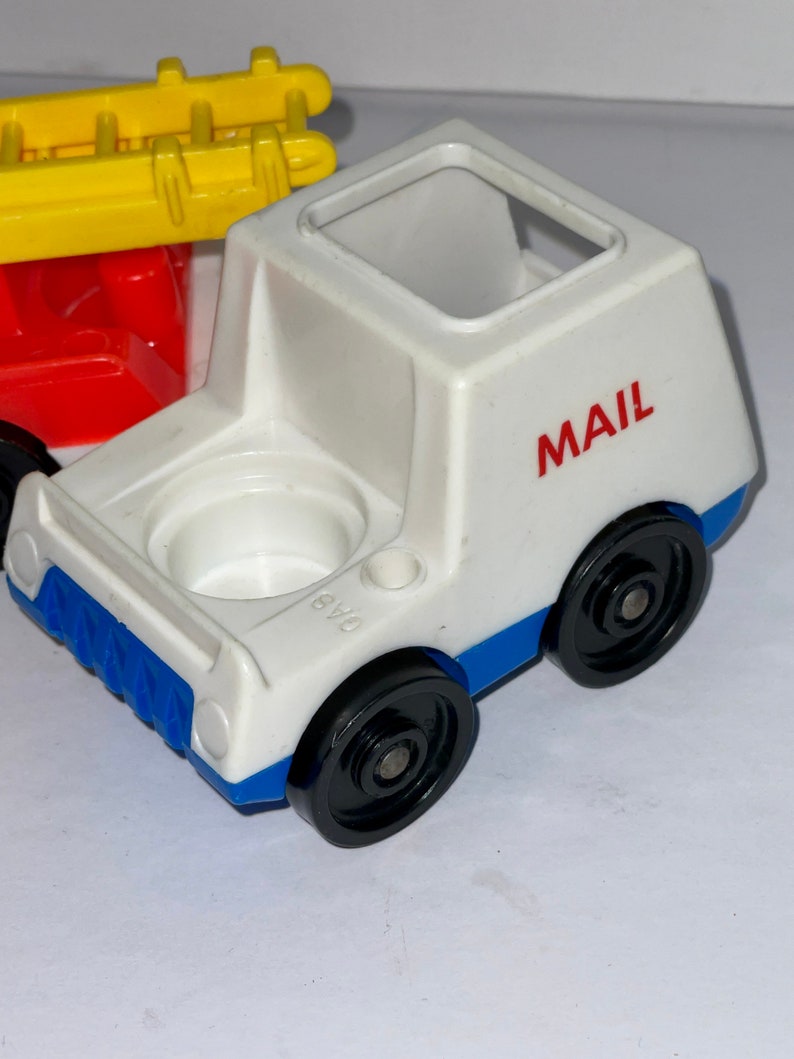 May include: White plastic toy mail truck with blue trim and black wheels. The truck has a red "MAIL" label on the side.