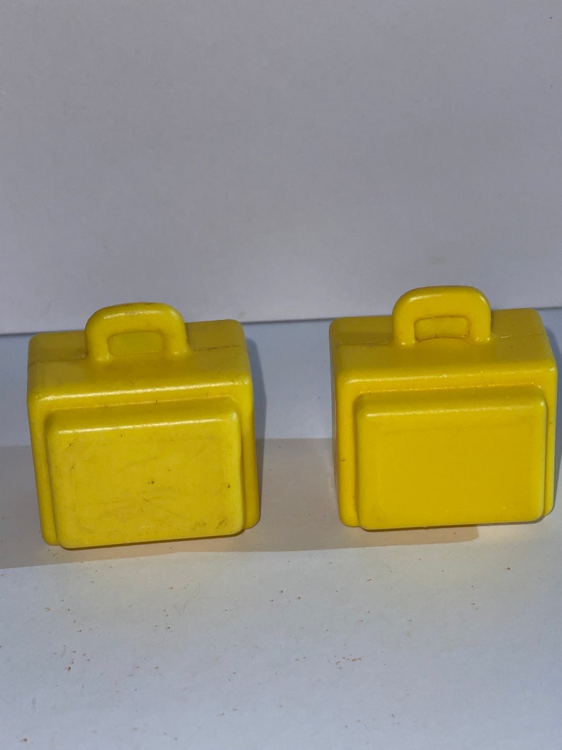 K&ouml;nnte beinhalten: Zwei gelbe Spielzeugkoffer aus Plastik mit Griffen. Die Koffer sind etwa 5 cm hoch und 5 cm breit.