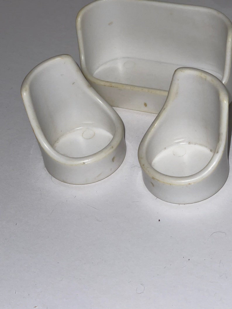 Puede incluir: Un conjunto de tres muebles de casa de mu&ntilde;ecas de pl&aacute;stico blanco, que incluye un sof&aacute; y dos sillas.