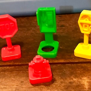 May include: A set of four plastic toy traffic signs, including a red stop sign, a green phone booth, a yellow parking meter, and a red fire hydrant.