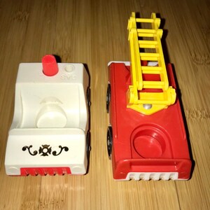 May include: Two vintage toy fire trucks. One is red with a yellow ladder and the other is white with a red cross and the word "GAS" printed on the side.