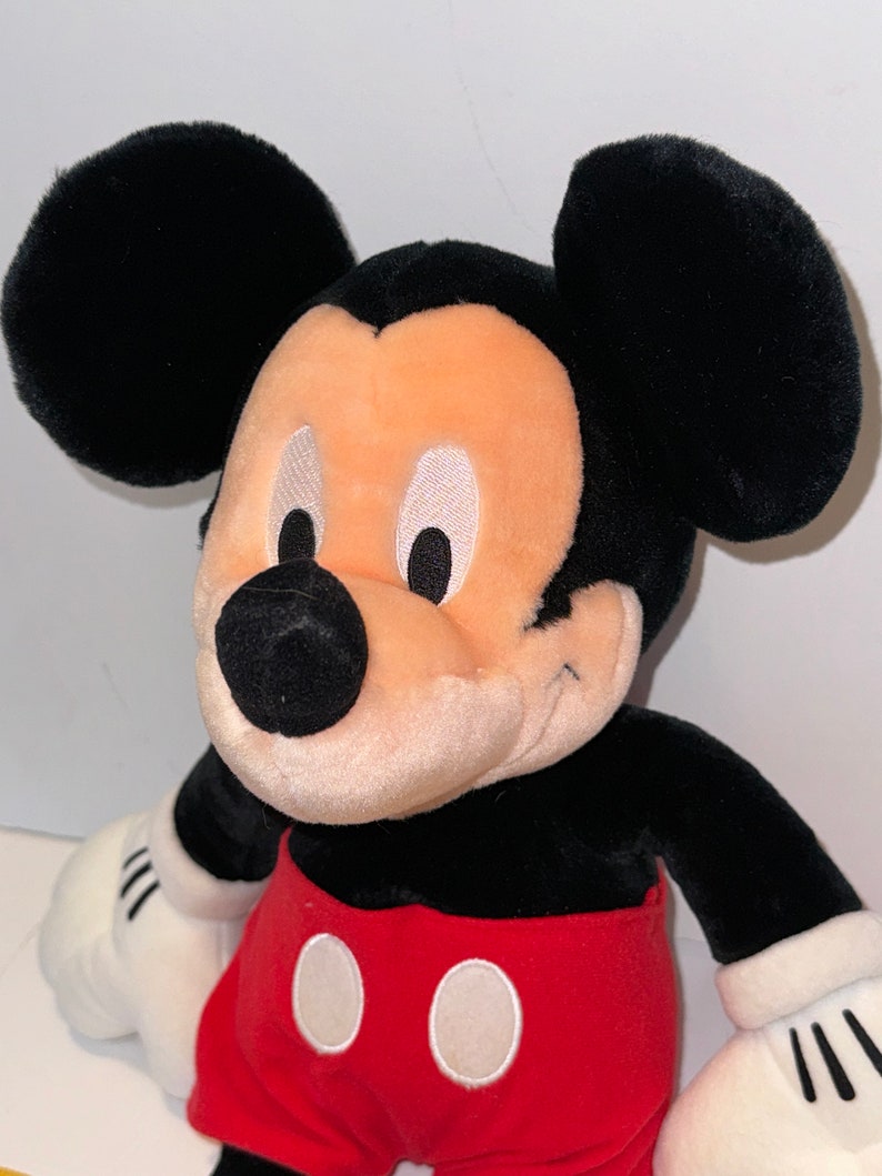 May include: A plush Mickey Mouse toy with black fur, large ears, and a red and white shorts. The toy has a smiling face with white eyes and a black nose.