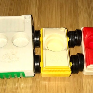 May include: Three vintage toy cars, one white with green trim, one yellow with white trim, and one red with white trim. Each car has black wheels and a small hole in the top. The cars are made by Little Tikes.