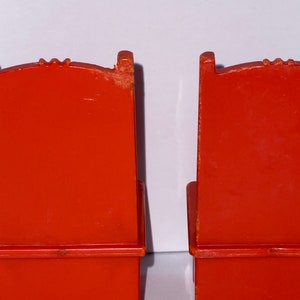 May include: Two red plastic chairs with a simple design. The chairs have a back, seat, and four legs.