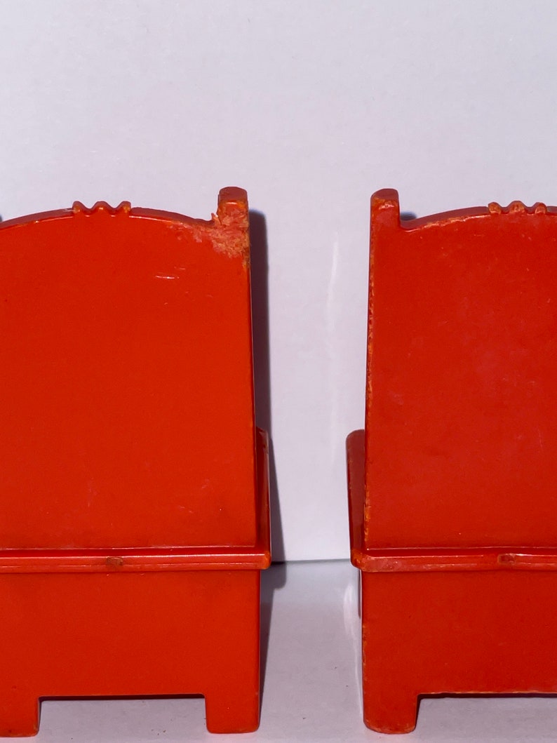 May include: Two red plastic chairs with a simple design. The chairs have a back, seat, and four legs.