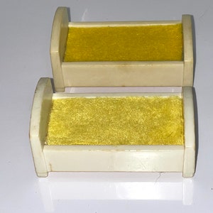 May include: Two white plastic doll beds with yellow fabric mattresses. The beds are stacked on top of each other.