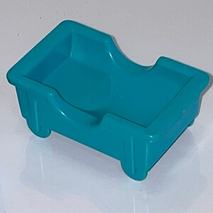 May include: A teal blue plastic toy bed with a curved headboard and two wheels on the bottom.