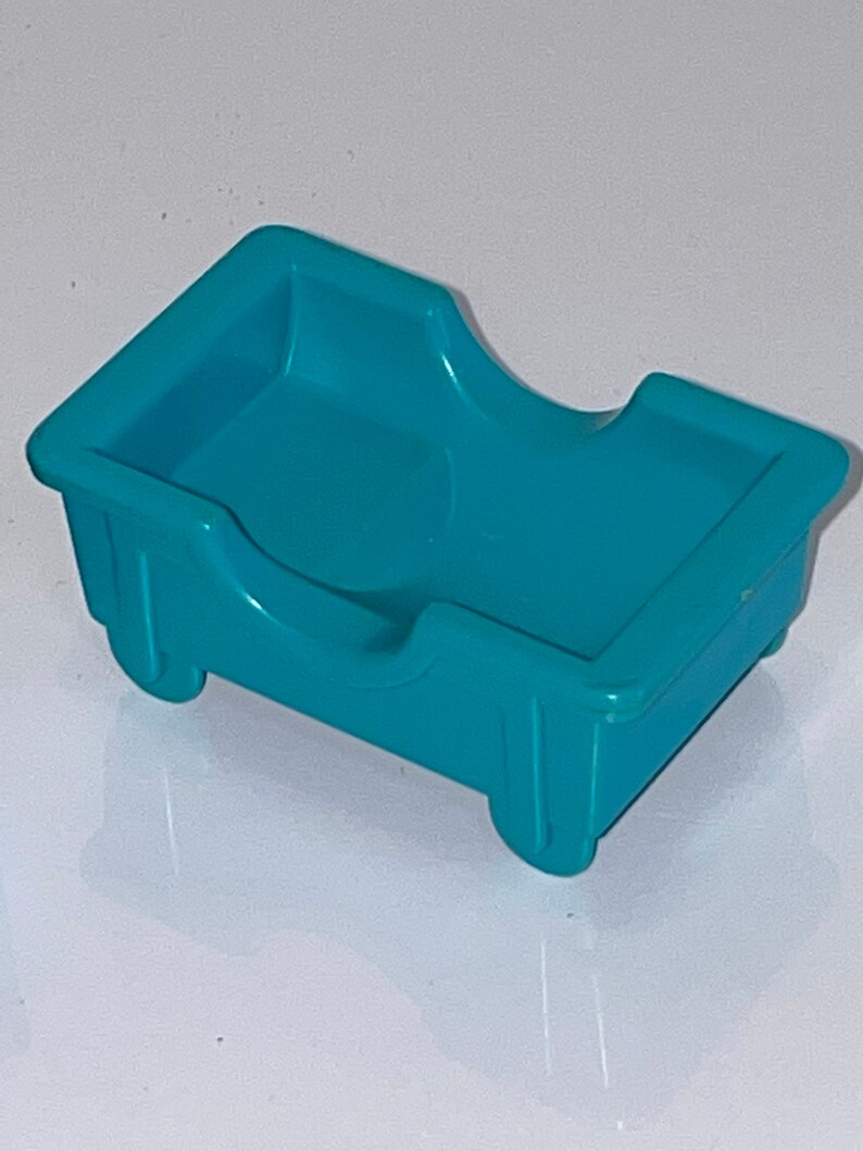 May include: A teal blue plastic toy bed with a curved headboard and two wheels on the bottom.