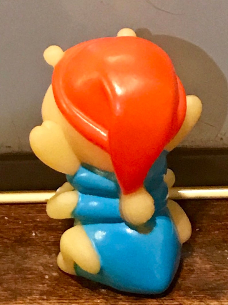 Puede incluir: Una peque&ntilde;a figura de pl&aacute;stico amarilla de Winnie the Pooh con un pijama azul y un gorro de dormir rojo.
