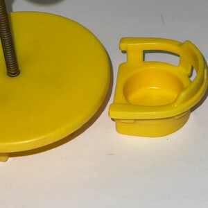May include: Yellow plastic toy table and chair set. The table is round and has a green plastic tree attached to the top. The chair has a high back and a seat with a hole in the centre.