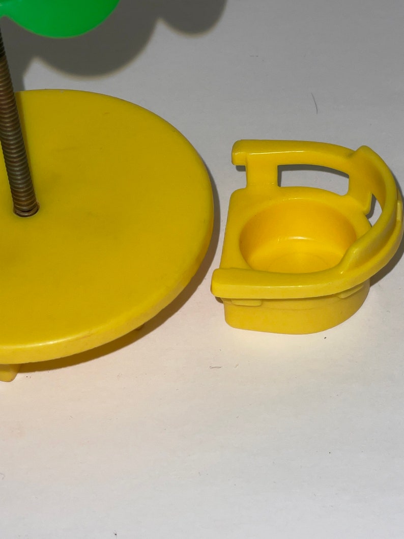 May include: Yellow plastic toy table and chair set. The table is round and has a green plastic tree attached to the top. The chair has a high back and a seat with a hole in the centre.