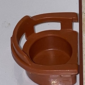 May include: A brown plastic toy chair with a rounded back and a small seat. The chair is designed to fit a small doll or action figure.
