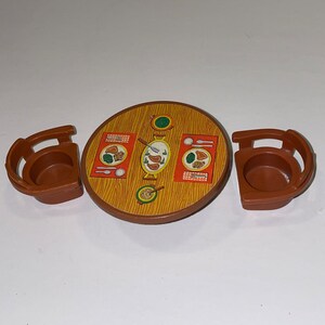 May include: A brown plastic toy table with a red and yellow printed design of plates with food. The table has three brown plastic chairs with a brown seat.