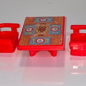 May include: A red plastic table and two chairs with a nautical themed design. The table top has a wood grain pattern with blue and yellow placemats featuring a sailboat and a lobster.
