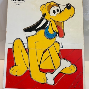 May include: A vintage Playskool wooden puzzle featuring Pluto, a yellow dog with black spots, a blue collar, and a red tongue. The puzzle has 7 pieces and is made in the USA. The text on the puzzle reads "Playskool 190-04 - 7 Pieces Pluto".