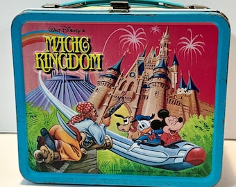 May include: Vintage blue metal lunchbox featuring Walt Disney's Magic Kingdom. The lunchbox has a colorful illustration of Cinderella's Castle, fireworks, and Disney characters including Mickey Mouse, Donald Duck, and a pirate.