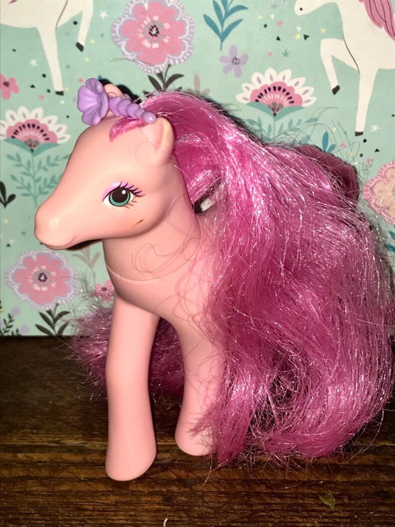 Puede incluir: Juguete My Little Pony rosa con un accesorio para el pelo de flor morada y pelo largo rosa.