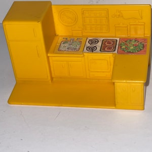 K&ouml;nnte beinhalten: Ein gelbes Spielzeug-K&uuml;chenset aus Plastik mit Sp&uuml;le, Herd, Backofen und Schr&auml;nken. Die K&uuml;che hat eine Uhr und ein Regal an der R&uuml;ckwand.