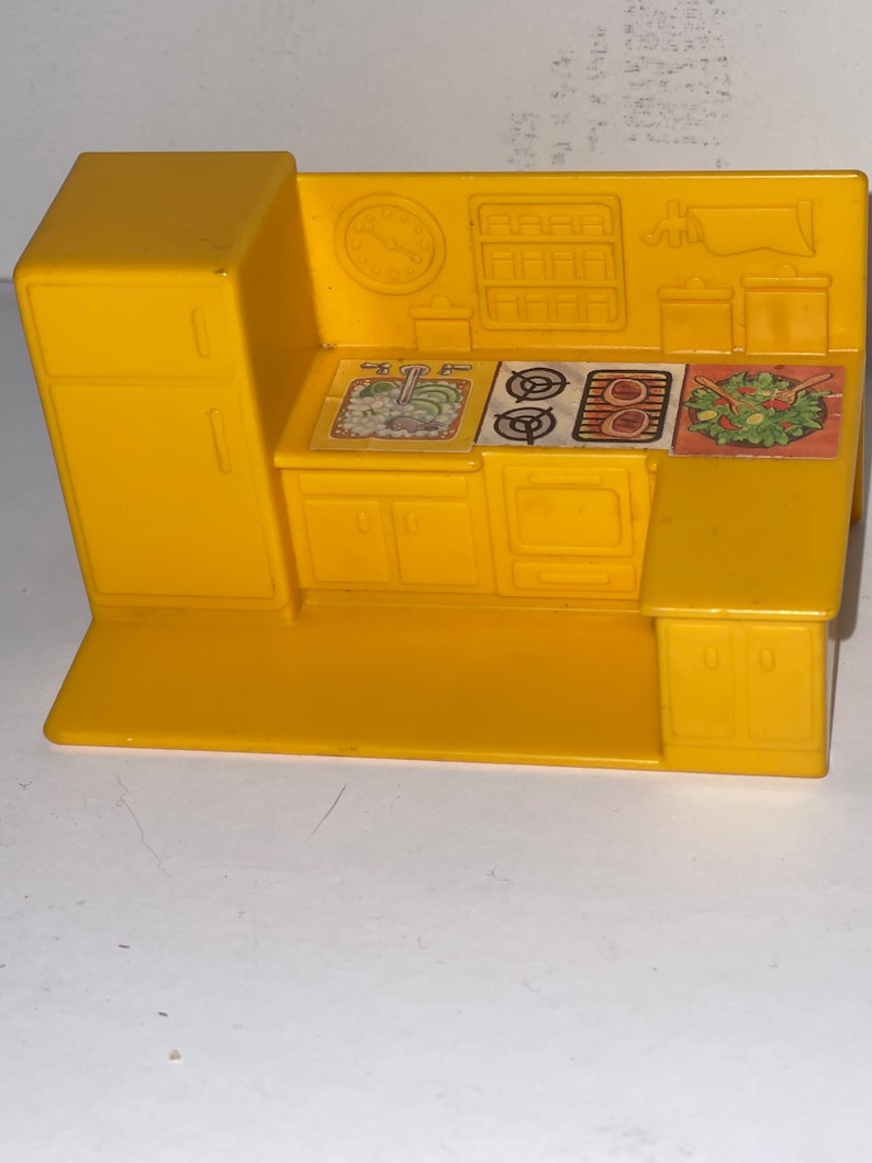 K&ouml;nnte beinhalten: Ein gelbes Spielzeug-K&uuml;chenset aus Plastik mit Sp&uuml;le, Herd, Backofen und Schr&auml;nken. Die K&uuml;che hat eine Uhr und ein Regal an der R&uuml;ckwand.