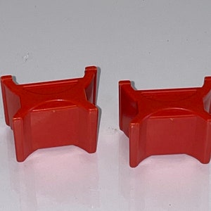 May include: Two red plastic toy blocks shaped like a table with four legs. The blocks are about 2 inches tall and 3 inches wide.