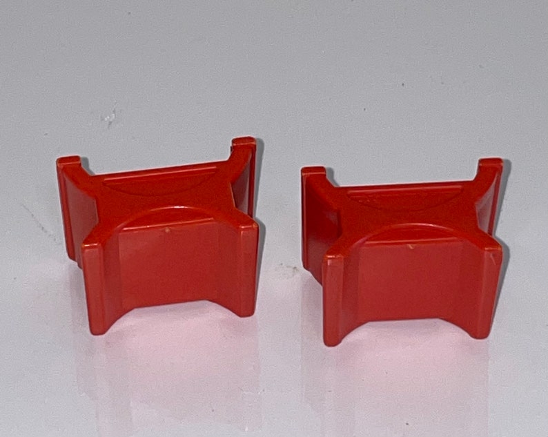 May include: Two red plastic toy blocks shaped like a table with four legs. The blocks are about 2 inches tall and 3 inches wide.