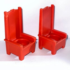 May include: Two red plastic chairs with a simple design. The chairs have a high back and a seat with a small hole in the center.