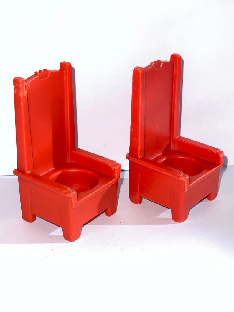 May include: Two red plastic chairs with a simple design. The chairs have a high back and a seat with a small hole in the center.