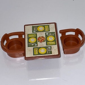 May include: A brown plastic toy table and two chairs. The table has a green and yellow patterned tabletop with a floral design and images of plates, forks, knives, and spoons.
